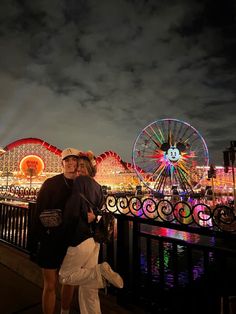 two people standing next to each other in front of a ferris wheel and carnival rides