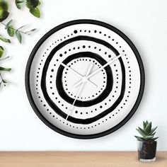 a black and white clock sitting on top of a table next to a potted plant