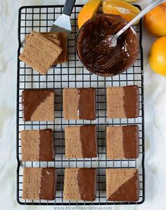 some crackers are sitting on a cooling rack with chocolate and oranges in the background