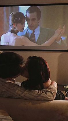 two people sitting on a couch in front of a large screen with a man and woman kissing