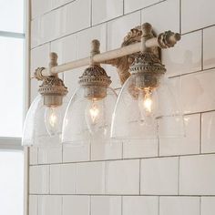 a bathroom light fixture with five lights on it's side and a white tiled wall in the background