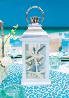 a white lantern sitting on top of a blue and white table cloth next to the ocean