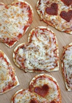 several heart shaped pizzas are arranged on a wooden table with cheese and pepperoni