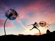 a silhouette of a person holding a stick and flying through the air next to a dandelion