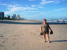 a woman standing on top of a sandy beach next to the ocean with buildings in the background