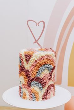 a multicolored cake sitting on top of a white plate next to a pink heart