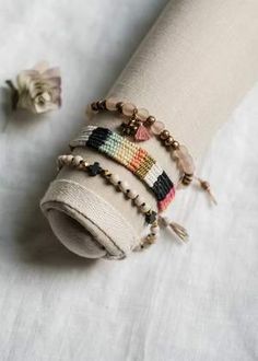 a stack of bracelets sitting on top of a white cloth covered table next to a flower