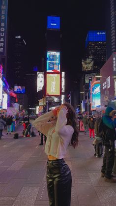 a woman standing in the middle of a busy city at night with her hands on her head