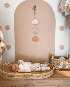 a baby laying in a wicker basket next to a wall with seashells on it