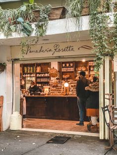 people are standing in the doorway of a store with plants hanging from it's roof