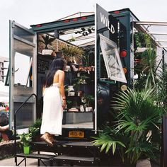 a woman is standing in the open door of a food truck with potted plants