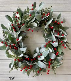 a christmas wreath with red berries and green leaves on a white wooden background, measurements