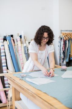 a woman is working at a table with fabric on it and scissors in her hand