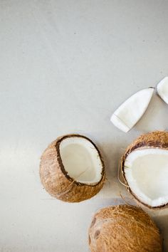 three whole coconuts and one cut in half on a white surface with two pieces missing