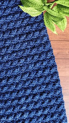 a blue crocheted dishcloth with green leaves on the side and a wooden table