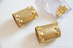 two pairs of gold studded earrings sitting on top of a white table next to each other