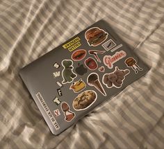 an open laptop computer sitting on top of a bed covered in lots of stickers