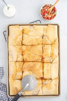 a pan filled with food on top of a counter next to a bowl of salsa