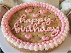 a birthday cake with pink frosting and hearts on it is being held by someone