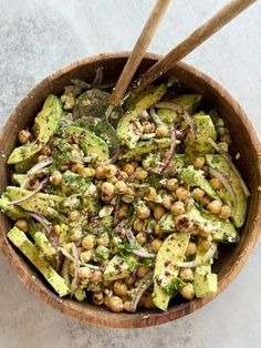 a wooden bowl filled with chickpeas and avocado salad next to two wooden spoons