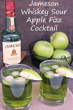 two glasses filled with green apple fizz next to an empty bottle and basket of apples