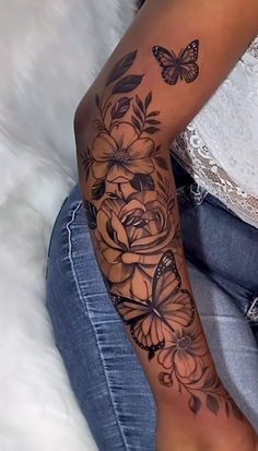 a woman's arm with flowers and butterflies on it, while she is sitting down