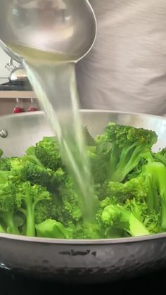 broccoli is being cooked in a pan with a ladle pouring water on it