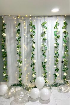 white balloons and greenery are on the floor next to an artificial curtain with lights