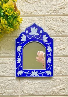 a blue and white mirror sitting on the side of a wall next to a potted plant