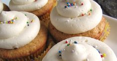 some cupcakes with white frosting and sprinkles on them are sitting on a plate