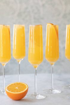 orange juice in wine glasses lined up with an orange slice on the side and another glass next to it