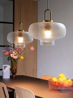 three lights hanging over a dining table with flowers and fruit in the bowl on it