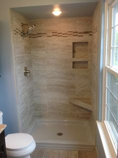 a white toilet sitting under a window next to a walk in bath tub and shower