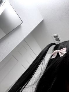 a woman with long black hair and a bow in her hair looking at herself in the mirror