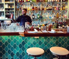 a man standing behind a bar with lots of bottles and glasses on top of it