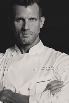 a black and white photo of a man in a chef's coat with his arms crossed