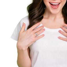 a woman is holding her hands on her chest and smiling at the camera while wearing a white t - shirt