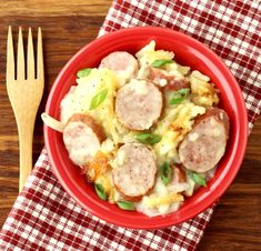 a red bowl filled with pasta and sausage on top of a checkered table cloth