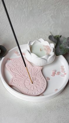 a white plate topped with a pink butterfly shaped candle holder and a black twig