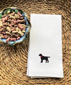 a dish towel with a black dog embroidered on it next to a bowl of dog treats