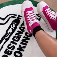 a person wearing pink tennis shoes on top of a white and green rug with black writing