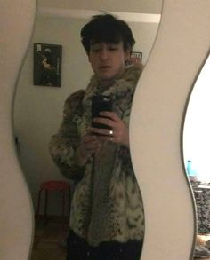 a man taking a selfie in front of a mirror wearing a fur coat and holding a cell phone