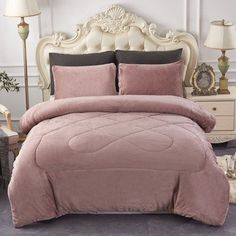 a bed with pink comforter and pillows in a room next to two lamps on either side of the bed