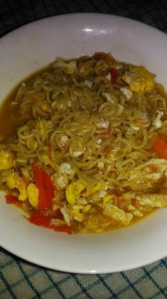 a white bowl filled with noodles and vegetables on top of a blue tablecloth covered table