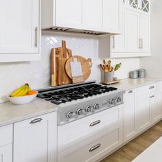 a kitchen with white cabinets and stainless steel stove top, cutting board on the burner