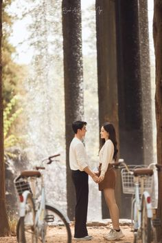 a man and woman standing next to each other holding hands in front of some trees