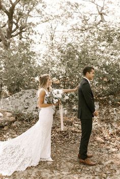 a bride and groom standing in the woods holding hands with each other as they look at each other