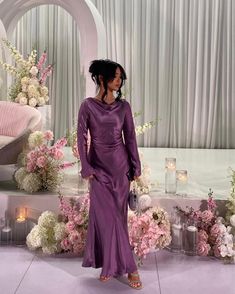 a woman in a purple dress standing on a stage with flowers and candles around her