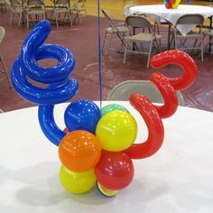 an assortment of colorful balloons on a table in a room with tables, chairs and other decorations