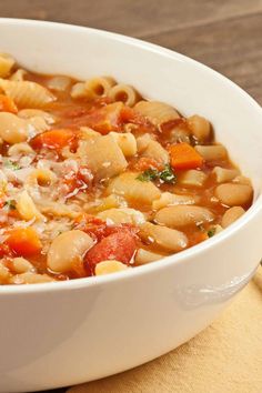 a white bowl filled with pasta and vegetables on top of a wooden table next to a napkin